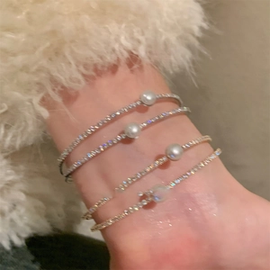 Detail of stacked double-layer bracelets with pearls and heart charms on female wrist