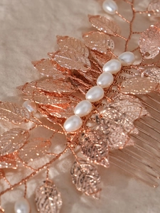Macro detail of rose gold leaf hair comb with pearls on a textured fabric background