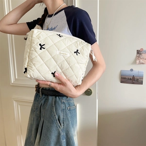 Detail of off-white quilted makeup bag featuring black embroidered bows and golden label