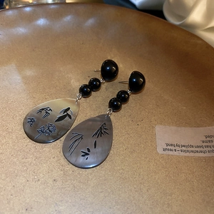 Macro shot of long drop earrings featuring black beads and engraved waterdrop pendants