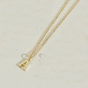 Detail view of gold letter A pendant necklace with refined link chain on stone background