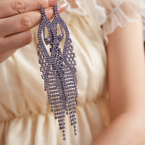 Detailed close-up of long purple rhinestone tassel earrings with a heavy luxury design
