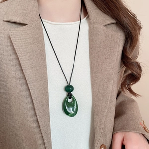 Detail of dark green teardrop pendant on black cord worn with a camel blazer