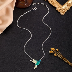 Detailed view of hummingbird pendant necklace with teal enamel on a satin background