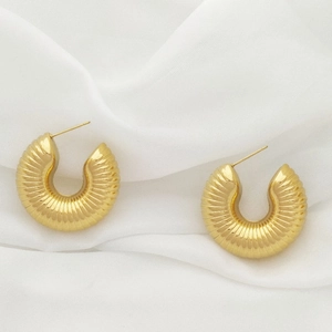 Detailed close-up of golden U-shaped earrings with textured spiral grooves on white silk