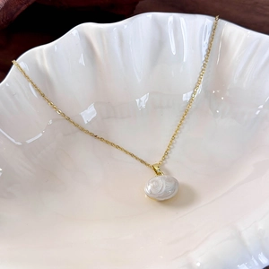 Macro shot of white enameled bean pendant on a golden chain in shell tray