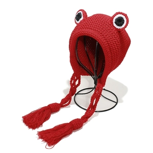 Close-up of red knit frog hat with large decorative eyes and braided tassel straps