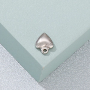 Polished silver stainless steel heart pendant on minimalist pedestal with focus on metallic luster