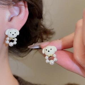 Close-up of white flocked puppy earrings with gold accents and elegant pearl rings