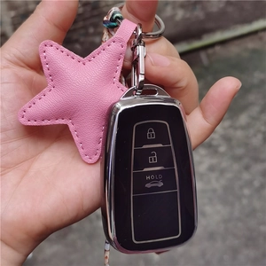 Pink star-shaped leather keychain charm held by hand next to a black car key fob