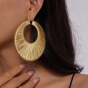 Close-up of a model wearing large golden woven textured hollow geometric round hoop earring