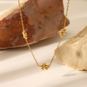 Collana in acciaio al titanio dorato con delicati ciondoli a fiore e cristalli
