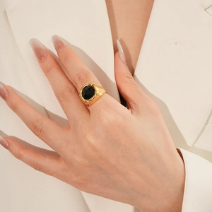 Dettaglio anello dorato vintage con pietra nera indossato da una modella in abito beige