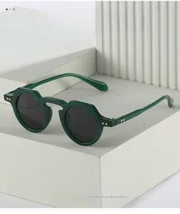 Detail of dark green geometric round sunglasses with gold rivets on textured stone pedestal
