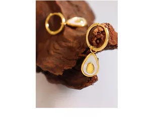 Macro detail of avocado shell earrings with gold metal and white enamel on wood texture