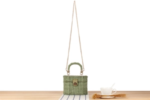 Detail of green straw woven box bag with metal lock and chain on wooden table
