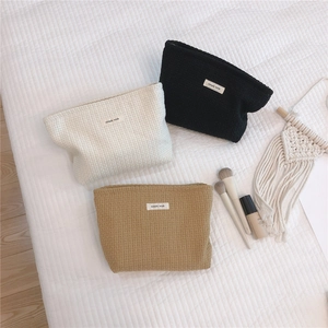 Three waffle textured woven cosmetic bags in beige, black and khaki on a white surface