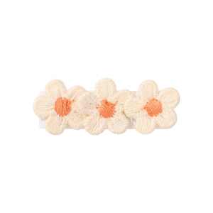 Detailed macro of white daisy floral embroidery on white ribbon-wrapped hair clip