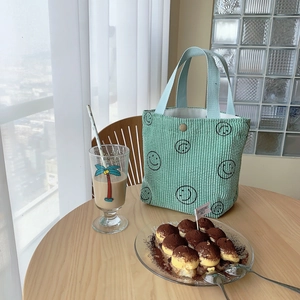 Detail of mint green corduroy tote bag featuring smiling faces and metal snap closure