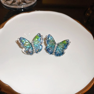 Détail de boucles d'oreilles papillon avec ailes dégradées bleu-vert et perle blanche