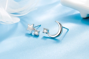 Macro shot of silver S925 star and moon earrings with cubic zirconia on blue silk