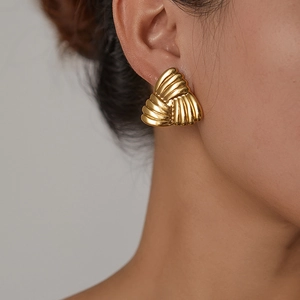 Close-up of golden geometric triangle stud earrings with textured wavy surface on model