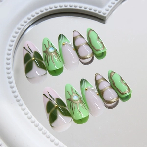 Green almond press-on nails with 3D gold details, pearls, and gemstone sun patterns