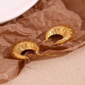 Detailed view of gold plated hollow oval earrings with rhombus pattern on brown paper