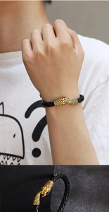 Close-up of black braided leather bracelet with golden snake head and red eye details