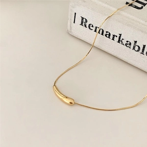 Close-up of a minimalist gold teardrop pendant on a fine chain over a white book