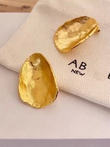 Close-up of golden irregular textured earrings with a logo canvas drawstring pouch