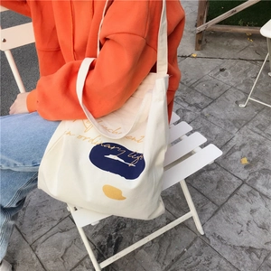 Detailed view of cream canvas tote bag featuring abstract blue and yellow art prints