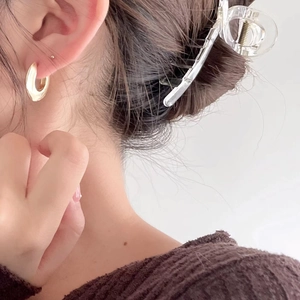 Close-up of a model wearing a thick golden hoop earring and a clear acrylic hair claw clip