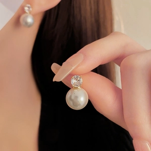 Détail de boucles d'oreilles clous en perle et zircone dorée sur l'oreille d'un mannequin