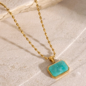 Detail of a gold bead chain necklace featuring a rectangular turquoise pendant on stone