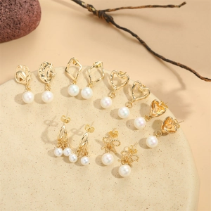 Set of six gold heart pearl earrings with bow and geometric designs on warm stone background