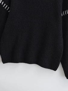 Dettaglio del maglione in maglia nera con cuciture bianche decorative e trama morbida