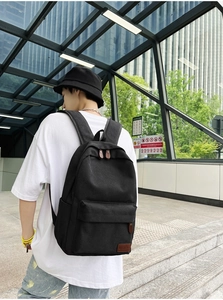 Detail of black canvas backpack with brown leather zipper pulls and logo patch