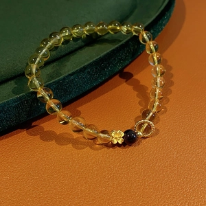 Close-up of yellow citrine bead bracelet with a gold flower charm on a velvet surface