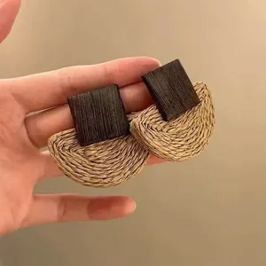 Detail of raffia woven semicircle and wooden block earrings on neutral background
