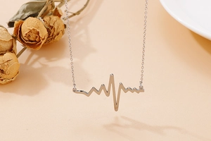 Detailed view of a silver heartbeat necklace with heart rate pendant on a warm background