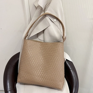 Brown woven leather shoulder bag displayed on a stylish trench coat for autumn fashion