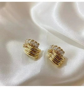 Macro shot of gold stud earrings with rectangular white zircons on silk background