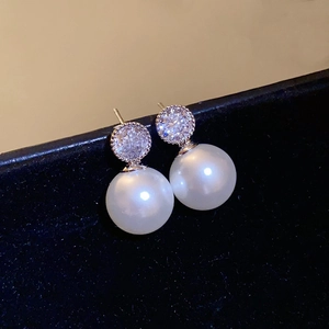 Macro shot of elegant pearl earrings with zircon cluster on black velvet display