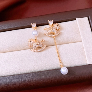 Macro detail of asymmetric 18k gold horse earrings with pearls and crystals