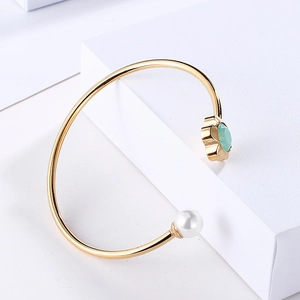 Detail of gold open bangle featuring white pearls and green crystal on geometric stairs
