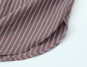 Detailed close-up of brown striped poplin shirt with curved hem and fine fabric texture