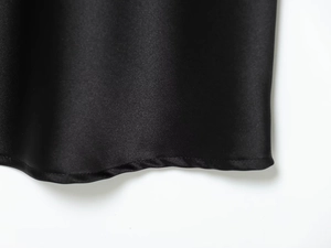 Macro detail of the smooth black satin fabric and high-quality hem stitching of the dress