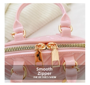 Detailed close-up of smooth dual golden zippers on a pink jelly shell bag with quilted texture