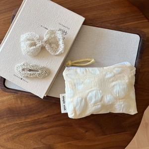 Détail d'une pochette en tissu beige à pois avec nœud en dentelle et pinces à cheveux